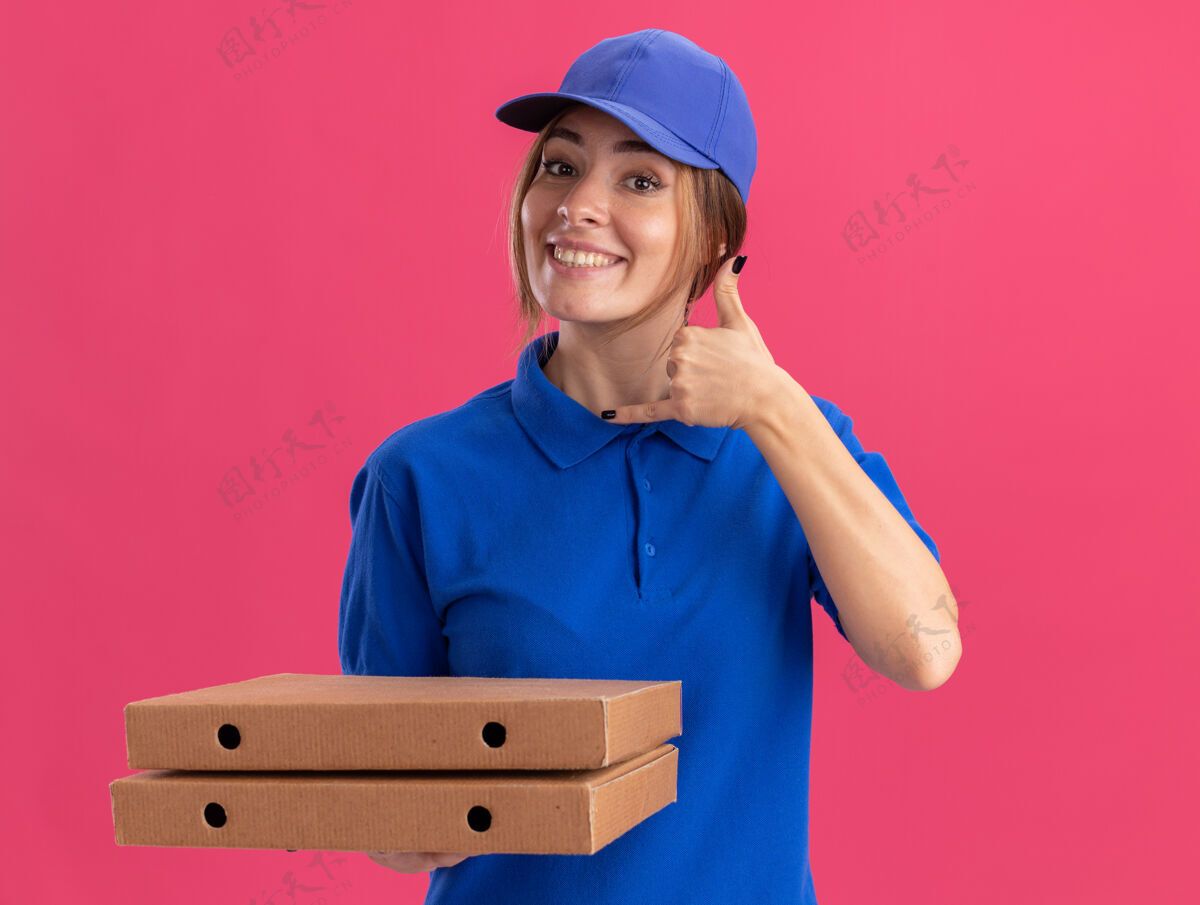 姿势微笑着的年轻漂亮的送货女孩 穿着制服 松着腰 拿着粉红色的比萨饼盒披萨手势盒子