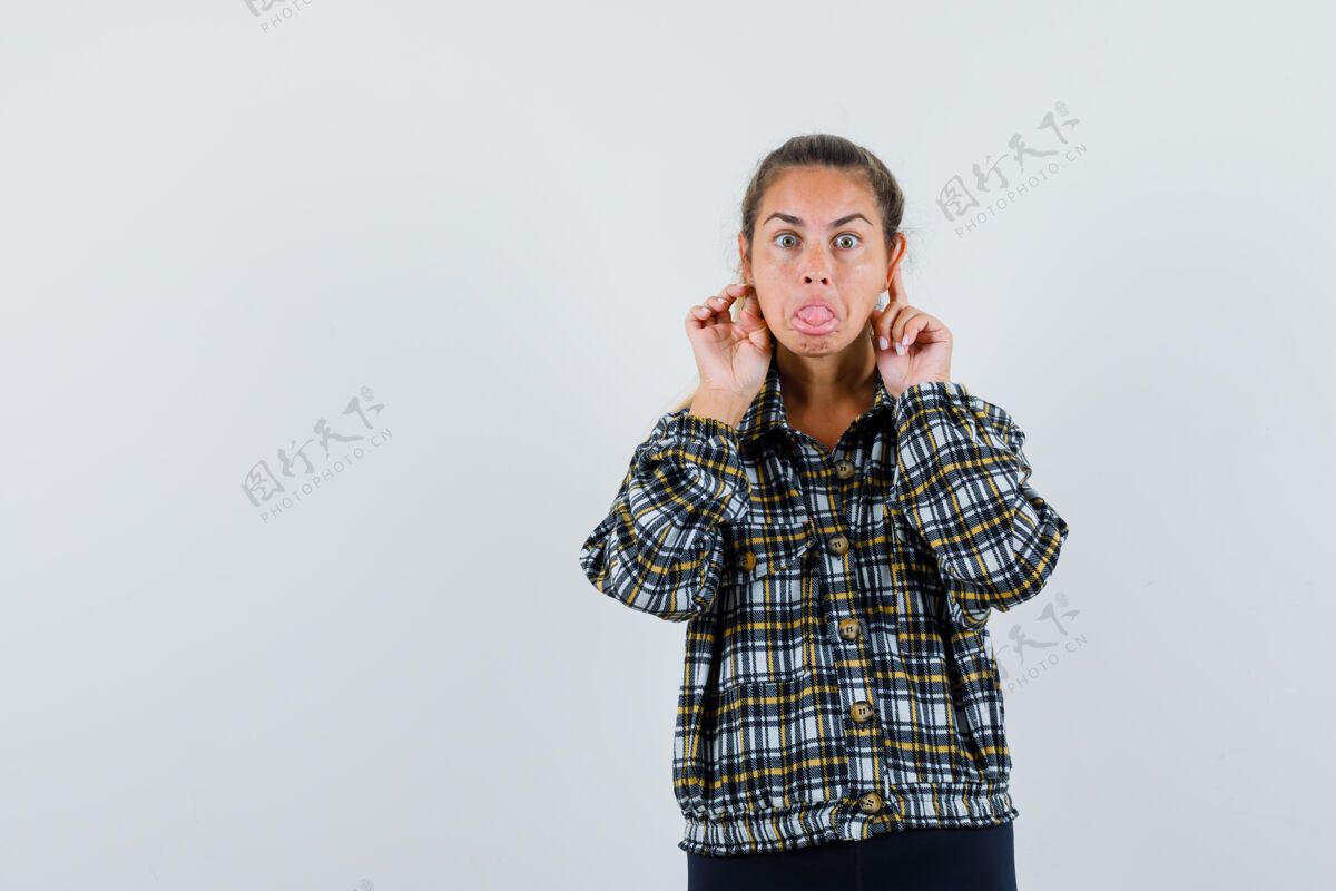 女孩穿着衬衫 短裤的年轻女性 手指放在耳朵后面 看起来很滑稽 正面视图手指衬衫持有