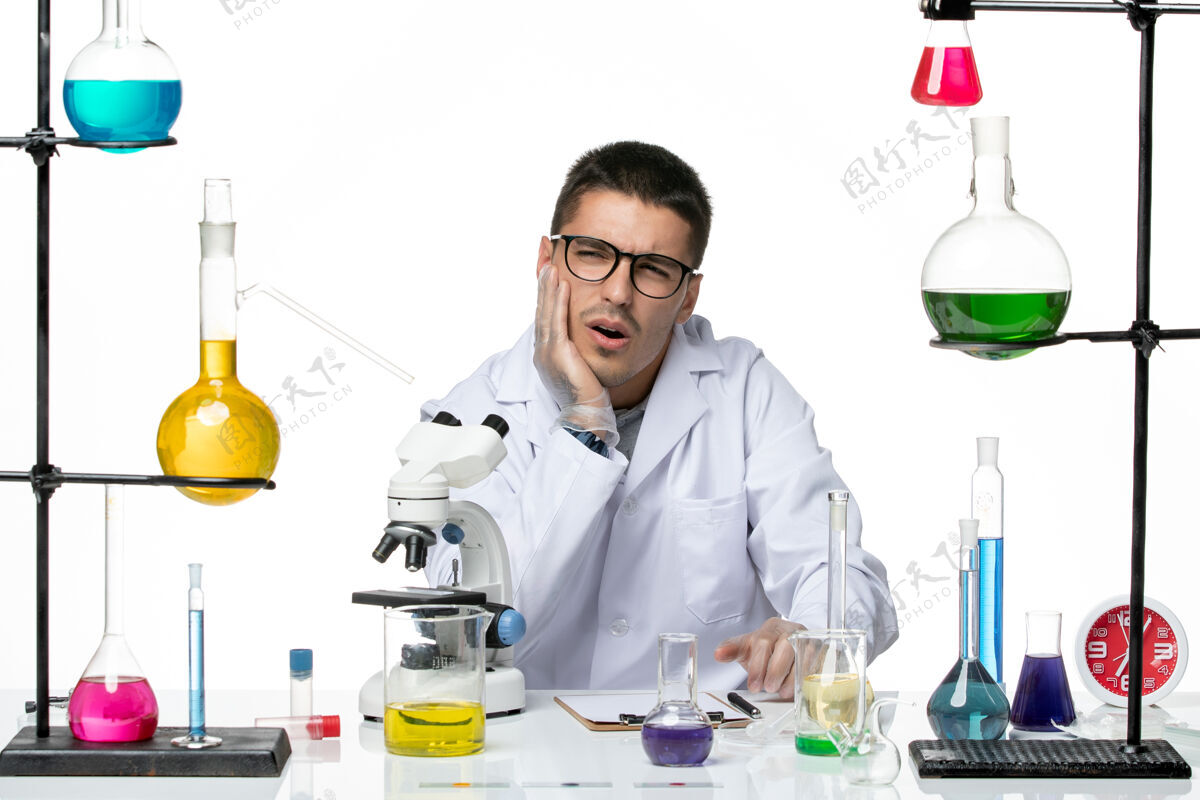 病毒前视图穿着白色医疗服的男性化学家坐在白色背景病毒实验室病毒-疾病科学的解决方案视图坐姿实验室外套
