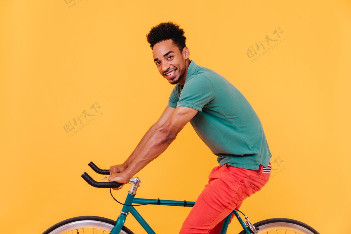 着装运动型的非洲黑发男人在自行车上摆姿势快乐的微笑的家伙在到处游荡休闲时髦自行车