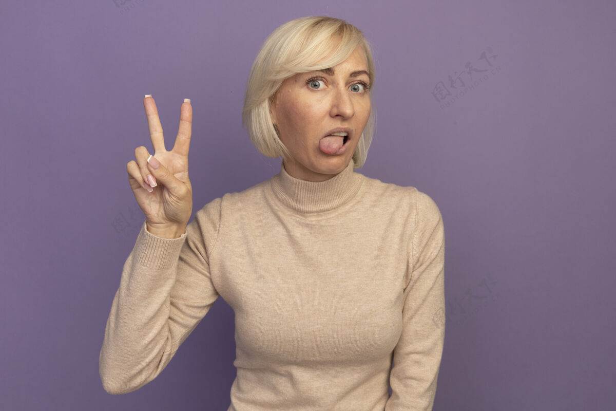 时尚令人印象深刻的金发斯拉夫女人stucks出舌头和手势胜利手标志紫色斯拉夫胜利成人