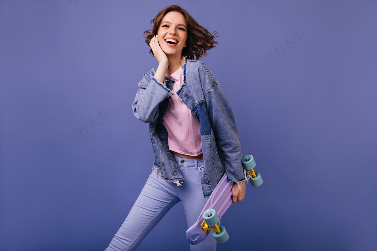 多彩穿着牛仔裤跳舞的幽默大笑的女人漂亮的高加索女孩拿着滑板的照片欢呼滑板休闲