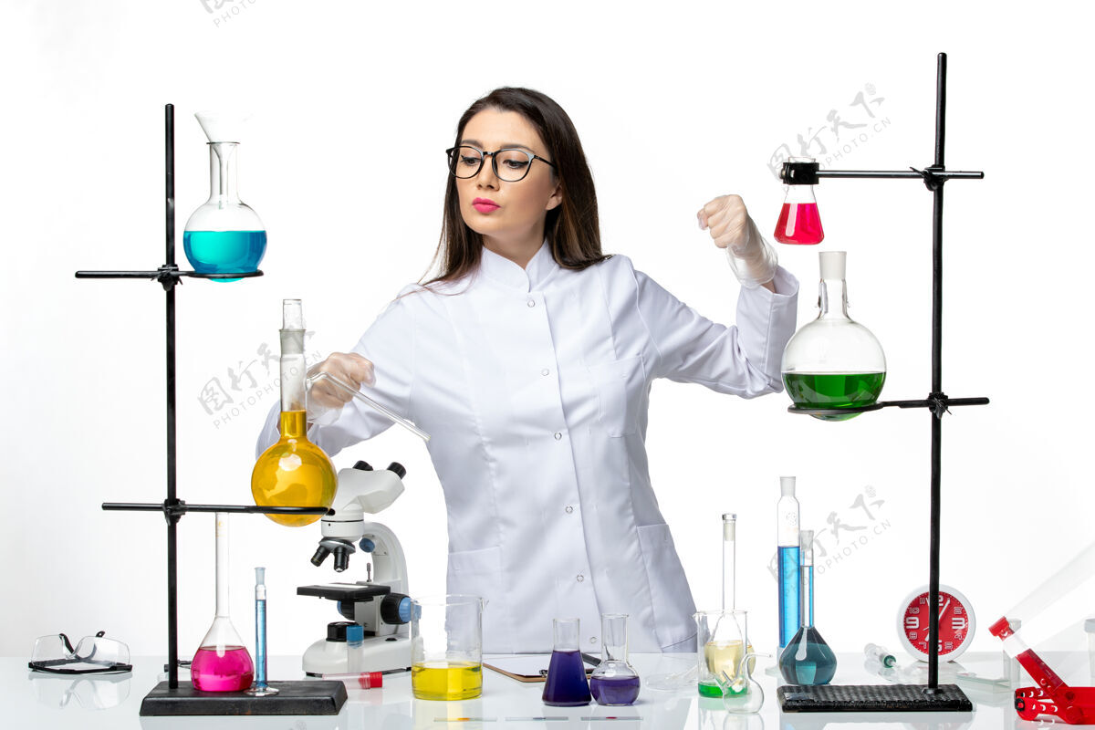 西装正面图：穿着无菌医疗服的女化学家站在桌子旁 拿着白色背景病毒疾病的解决方案 科维实验室大流行科学消毒家庭主妇医生