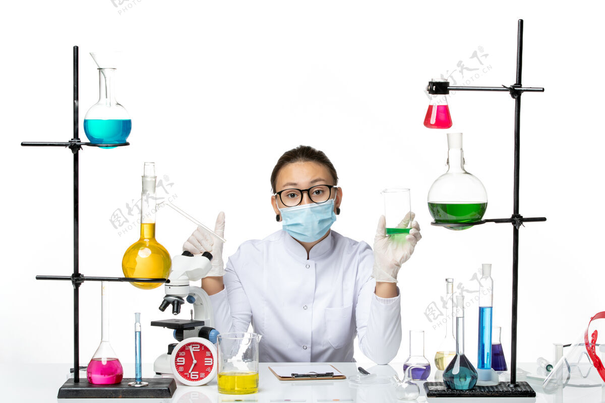 喷溅正面图白色办公桌上穿着医疗服的女化学家戴着口罩拿着溶液溅实验室病毒化学covid-实验室外套套装药物