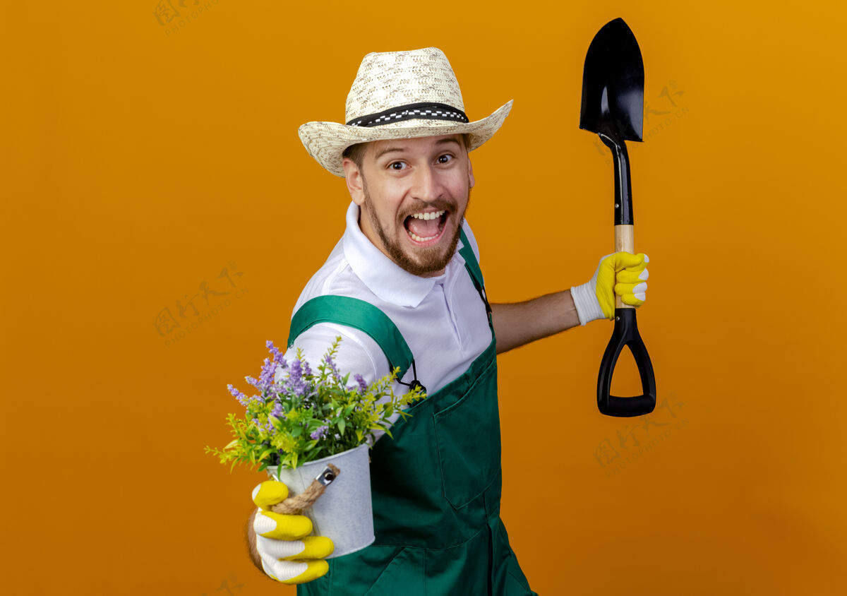 穿着印象深刻的年轻英俊的斯拉夫园丁穿着制服戴着帽子和园艺手套手持铁锹和花盆花园手套家伙