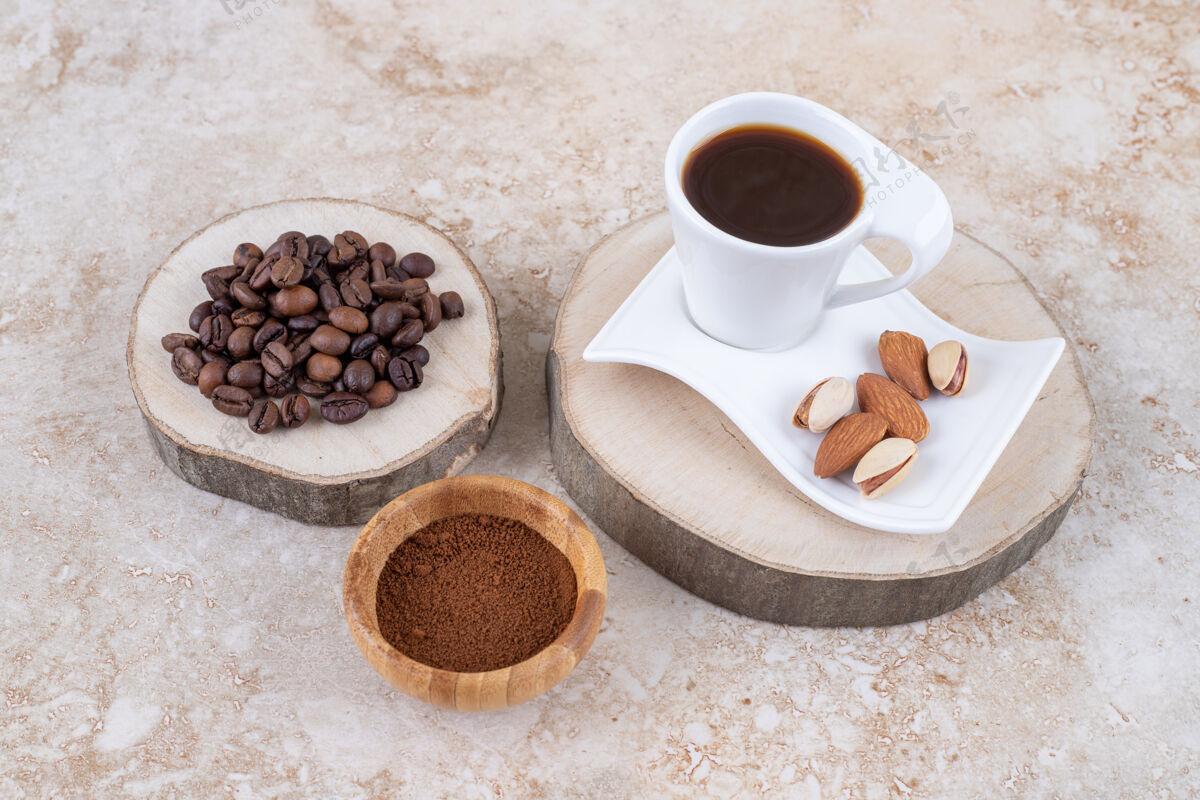美味一堆咖啡豆放在木板上 旁边是一小碗磨碎的咖啡和一杯杏仁开心果咖啡豆类咖啡磨碎的