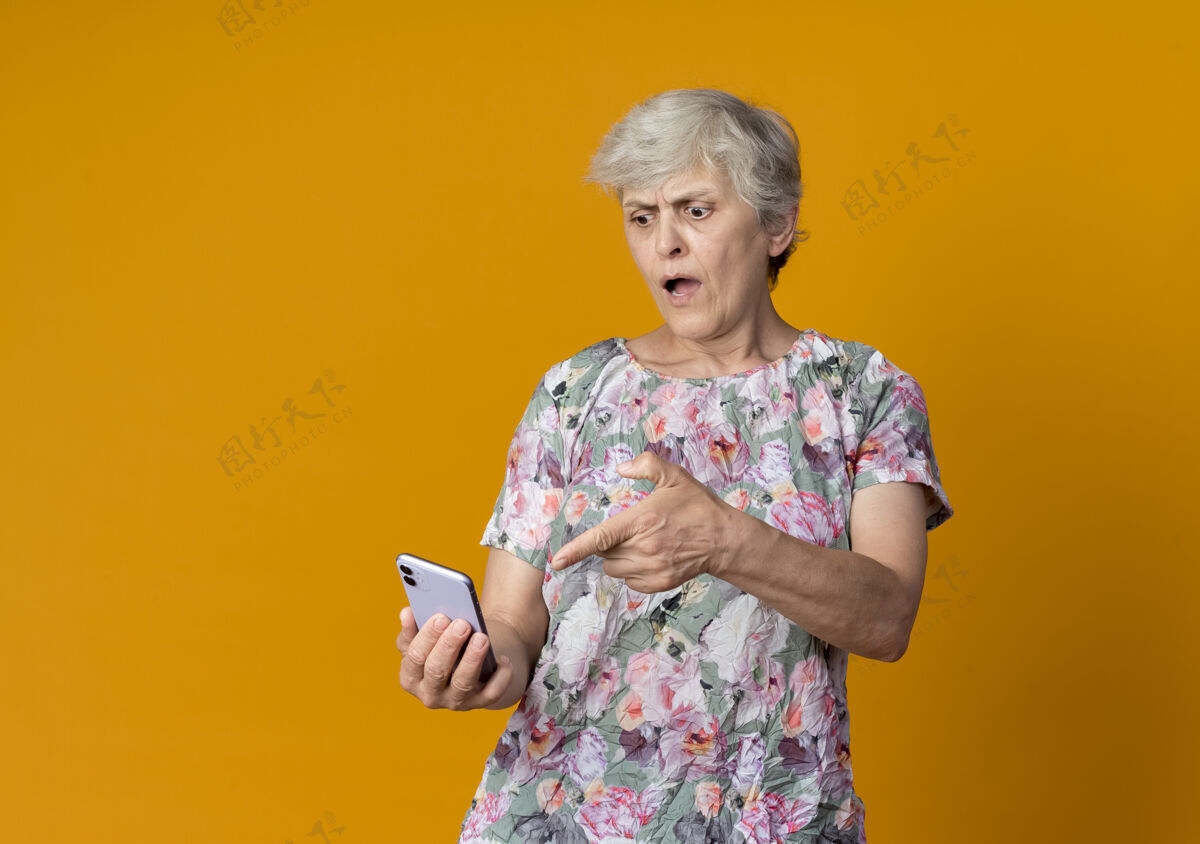 烦恼怒的老妇人拿着电话指着橙色墙上的电话女人点抱