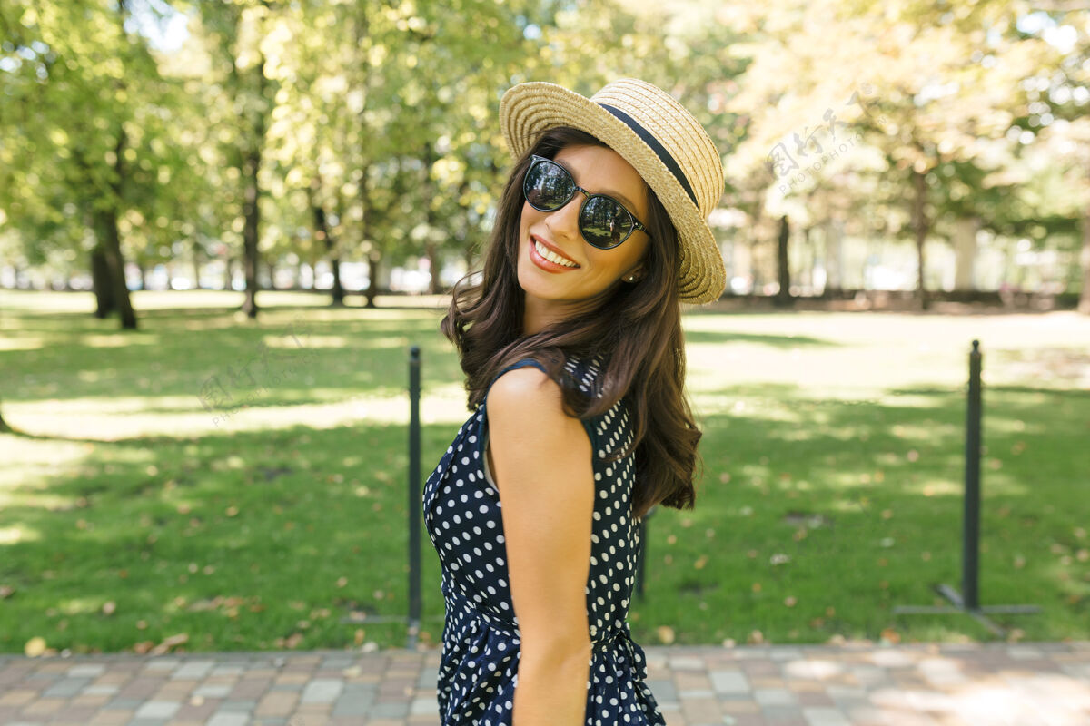 人一个迷人的女人戴着夏天的帽子 戴着黑色的太阳镜 穿着可爱的衣服 走在夏日公园里休闲积极特写