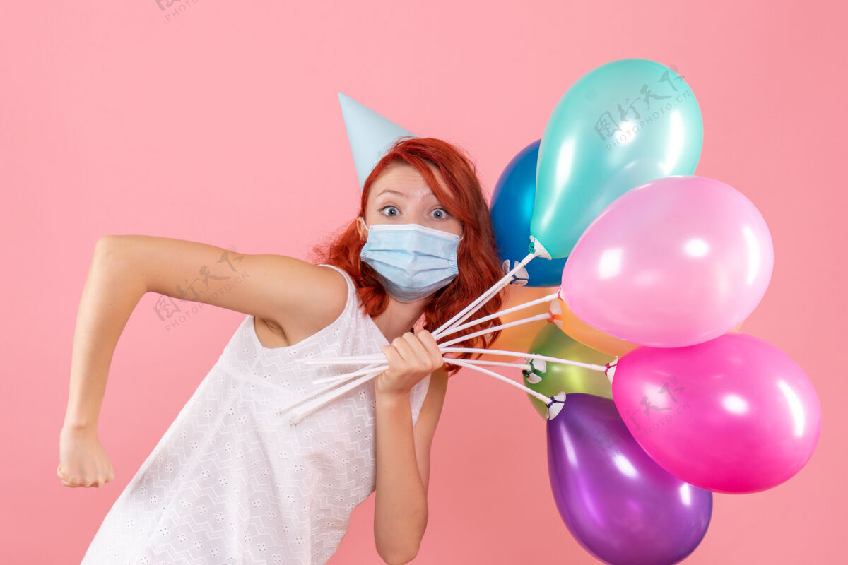 视图正面图年轻女性手持彩色气球在粉红色的面具上庆祝病毒圣诞节