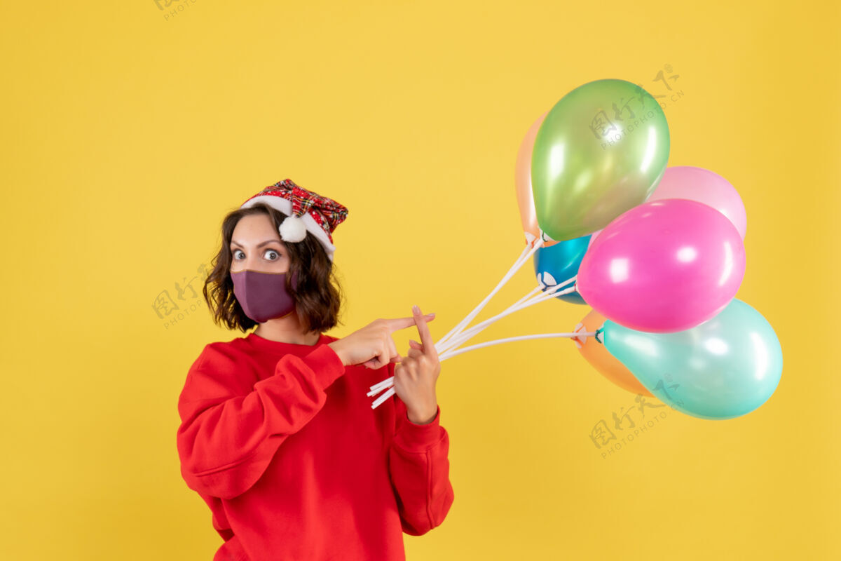 多彩正面图年轻女性拿着气球 戴着黄色的无菌面具年节日快乐