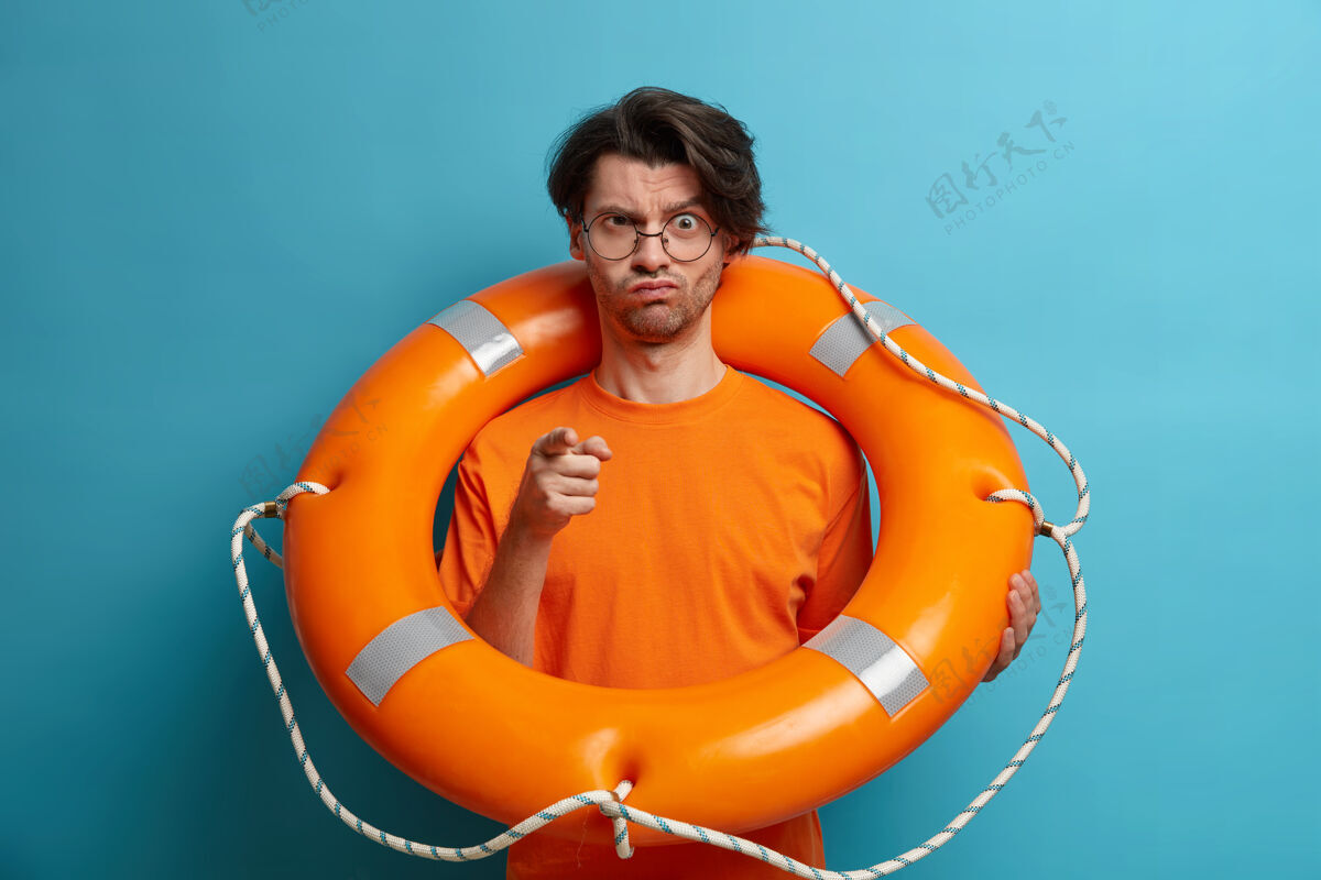 季节严重不满严格的男子救援人员指向你并警告水上的危险 与救生圈合影 在热带海滩工作 身着橙色t恤 准备救出沉没的人橙色人游泳