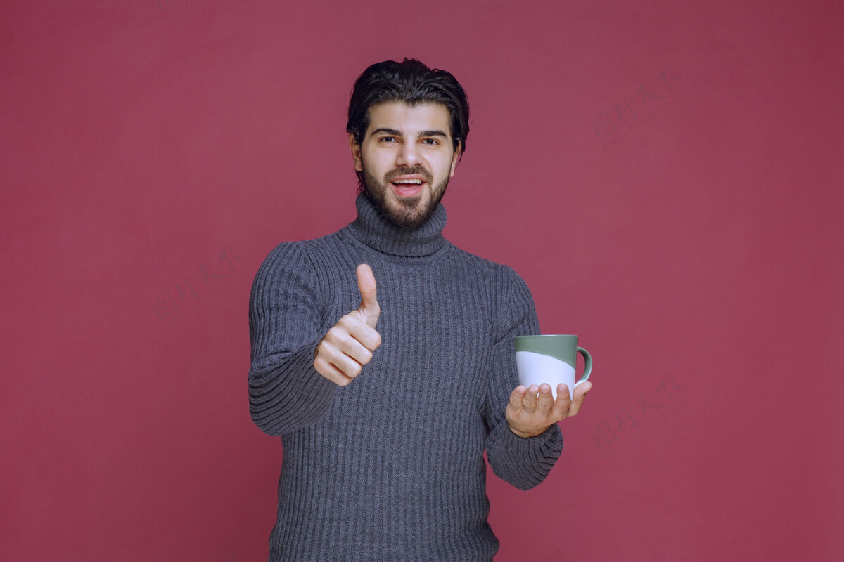 阳刚穿着灰色毛衣的男人拿着咖啡杯 享受着咖啡的味道聪明年轻模特