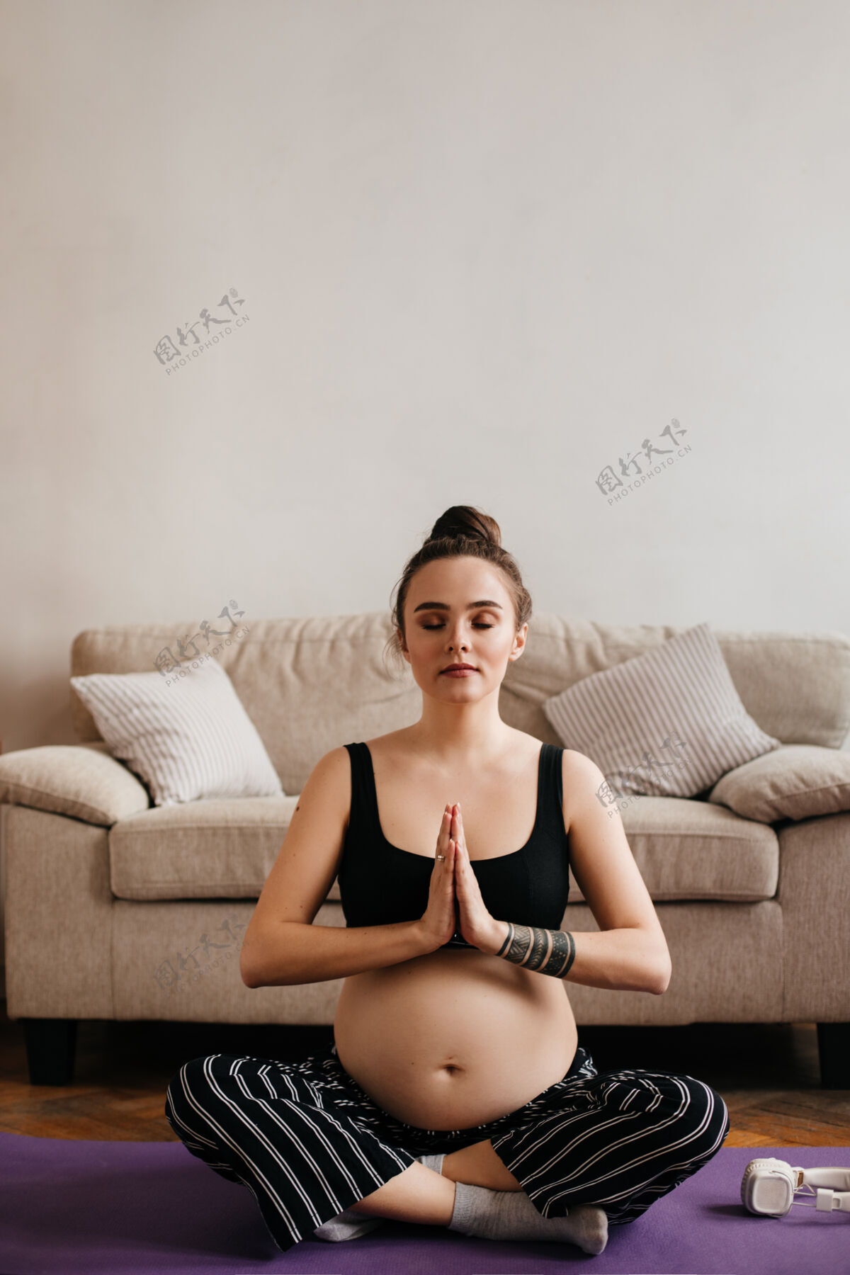 美丽冷静的黑发孕妇穿着上衣和条纹裤在客厅冥想和做瑜伽哑铃室内孕妇