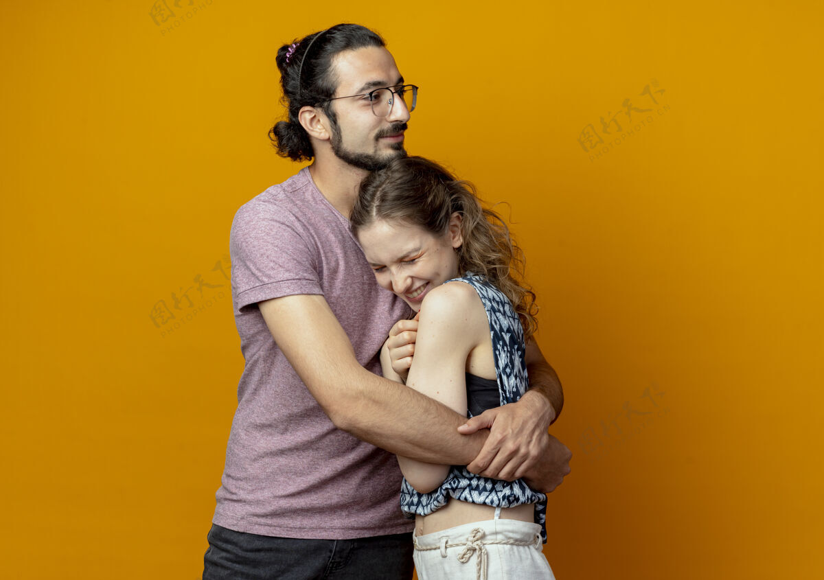 站着年轻漂亮的情侣男女在爱情中幸福地拥抱在一起站在橙色的背景下情侣拥抱年轻