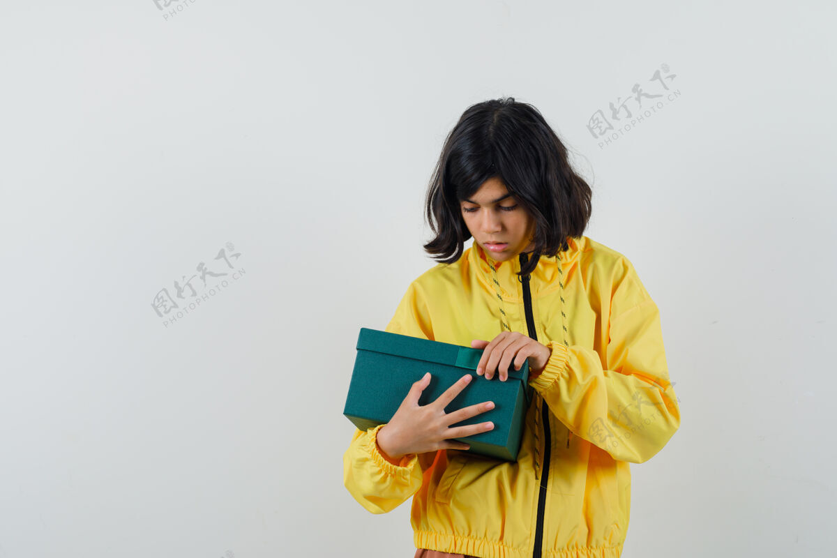 微笑小女孩试图打开礼物盒在黄色连帽衫 并期待好奇前视图盒子年轻欢呼