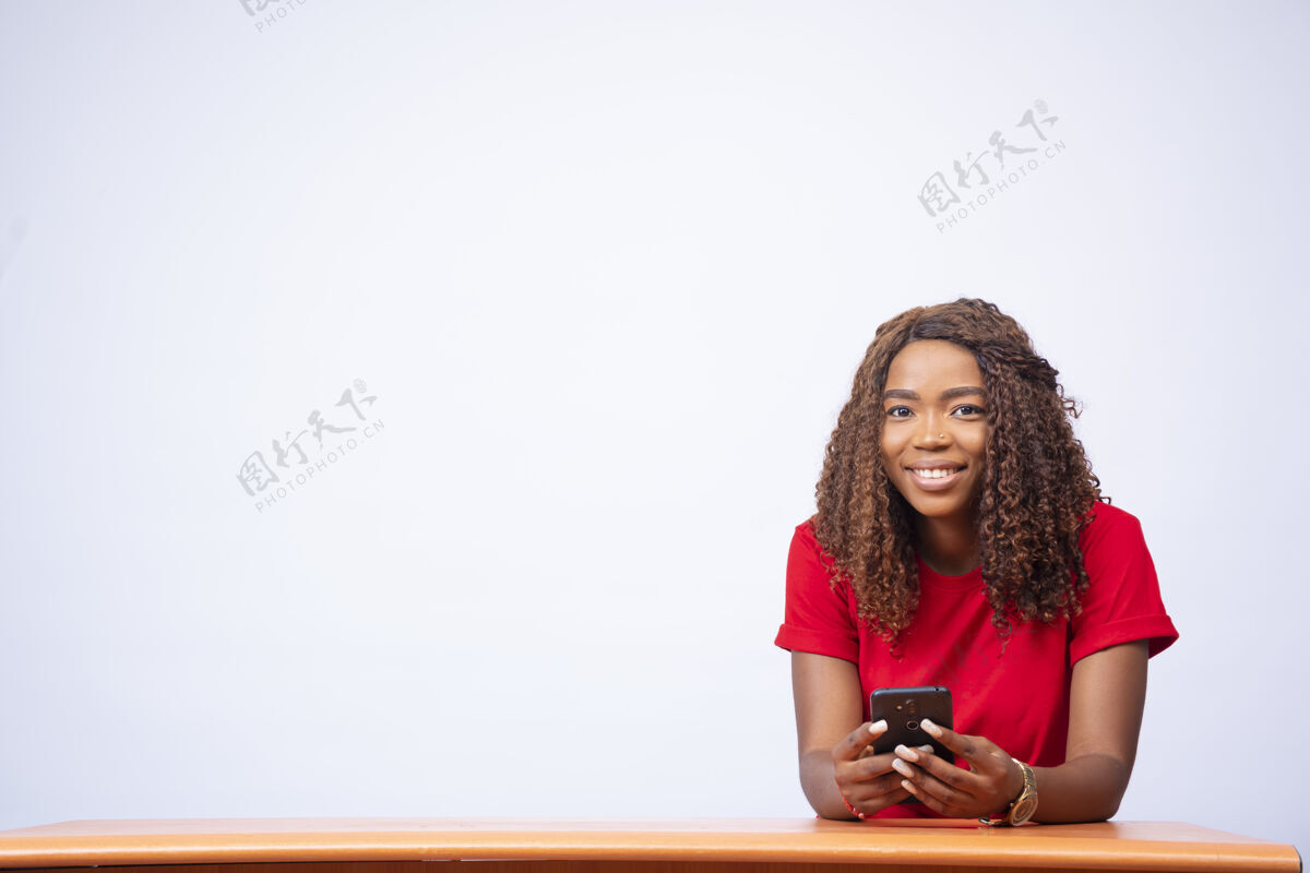 非洲年轻漂亮的黑人女士坐在办公桌前用手机微笑年轻女人