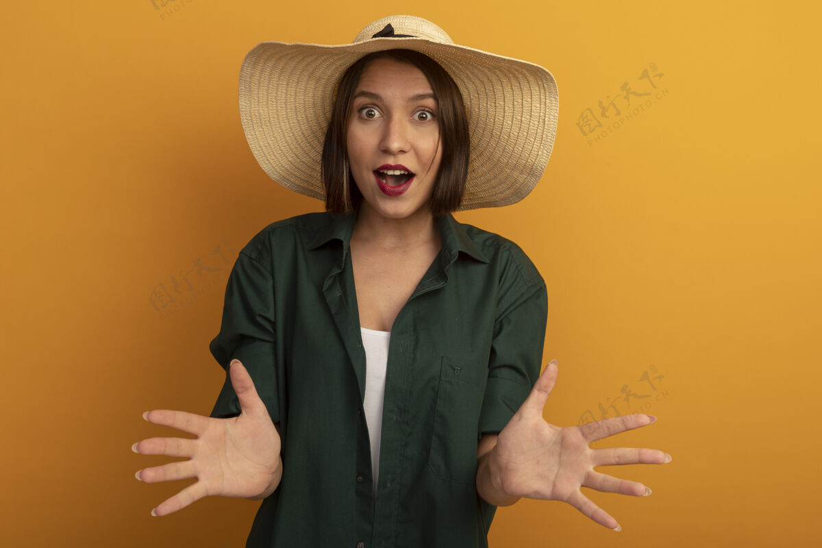 衣服一个戴着沙滩帽的漂亮女人在橙色的墙上张开双手手海滩人