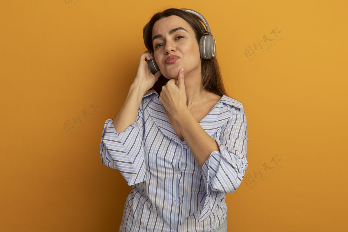脸戴着耳机的可爱女人把下巴隔离在橙色的墙上衣服表情市民