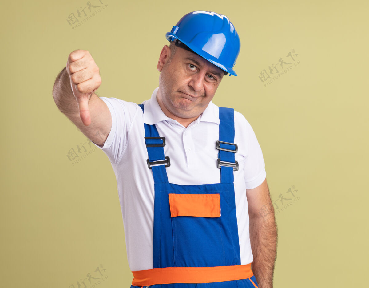 人失望的成年建筑工人穿着制服 大拇指朝下 被隔离在橄榄绿的墙上感觉表情人