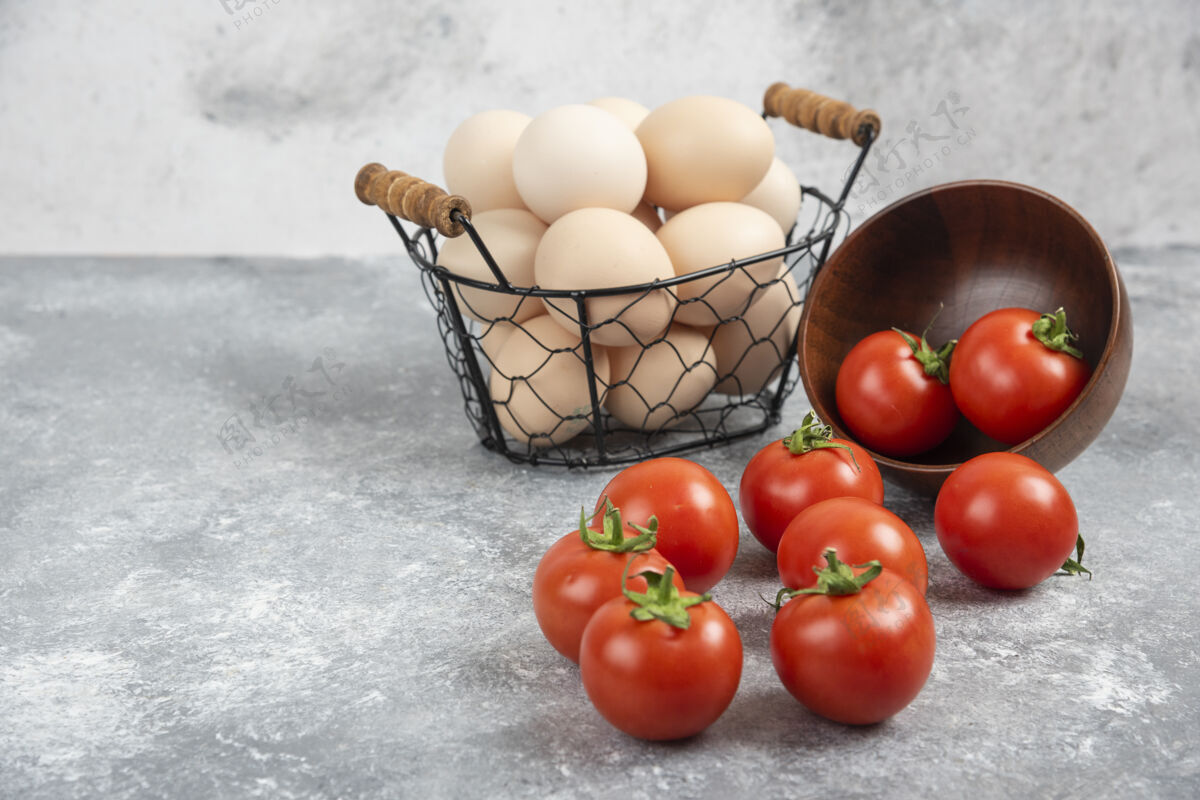 烹饪柳条篮子的生有机鸡蛋和一碗西红柿放在大理石上菜肴番茄贝壳