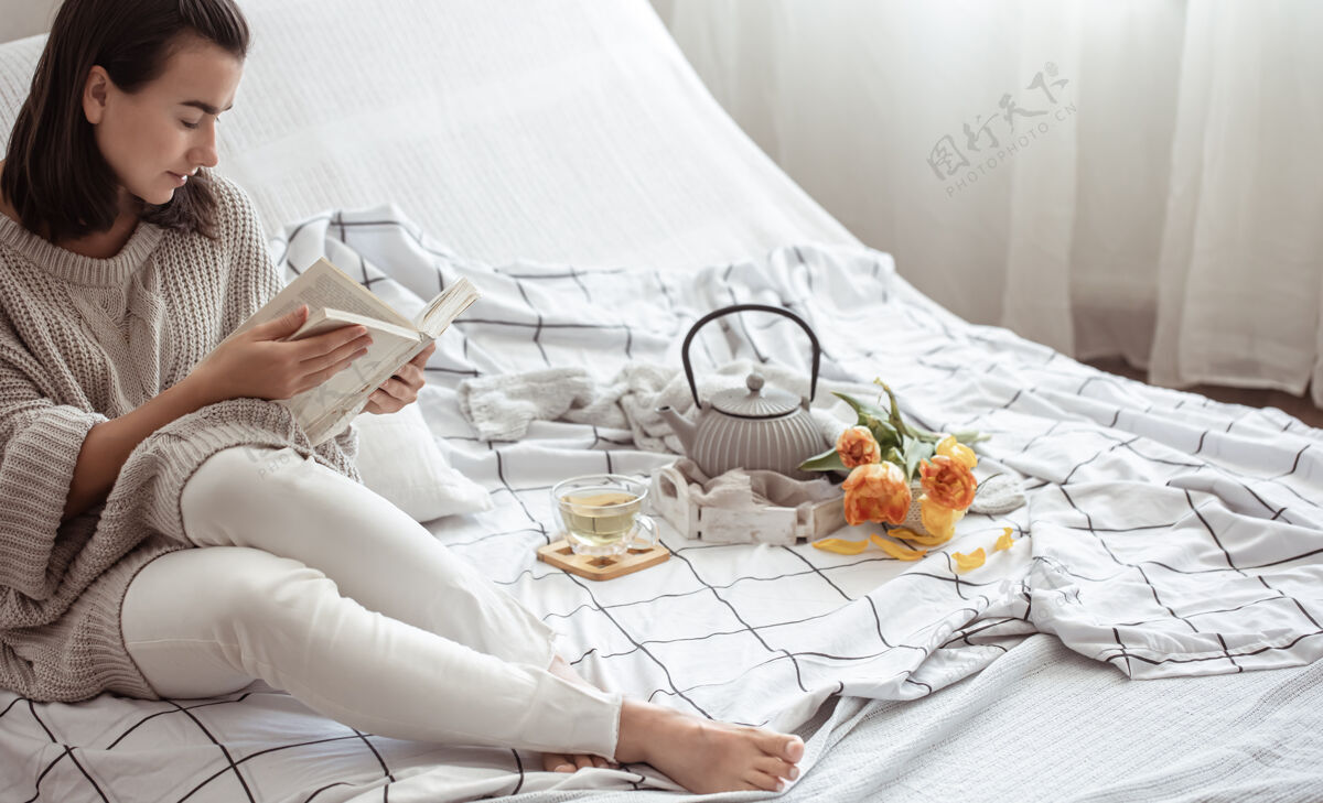 房子一个女人在床上休息 茶 一本书和一束郁金香春天的早晨和周末的概念舒适花女人