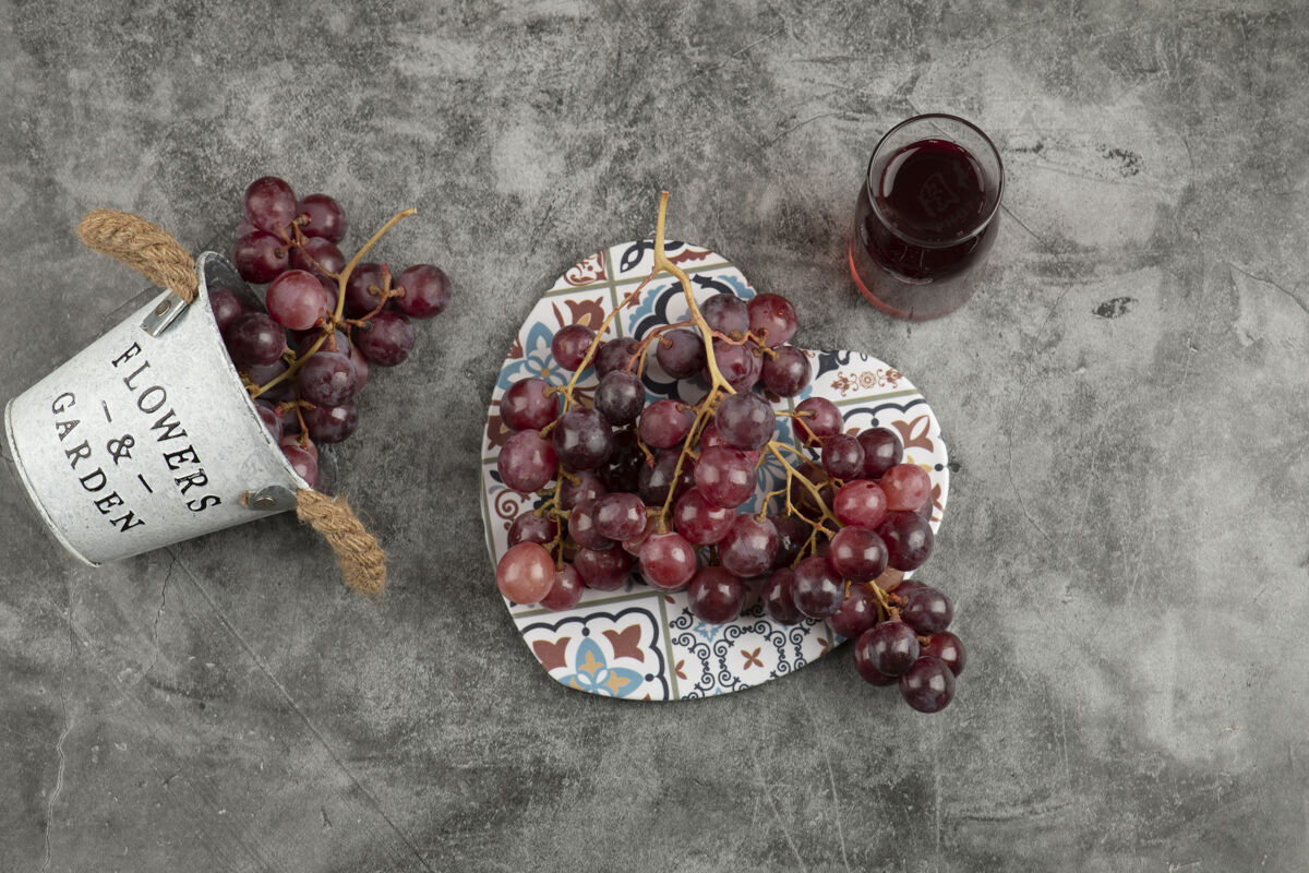 桶大理石桌上放着一桶红色的新鲜葡萄和一杯果汁葡萄平铺新鲜