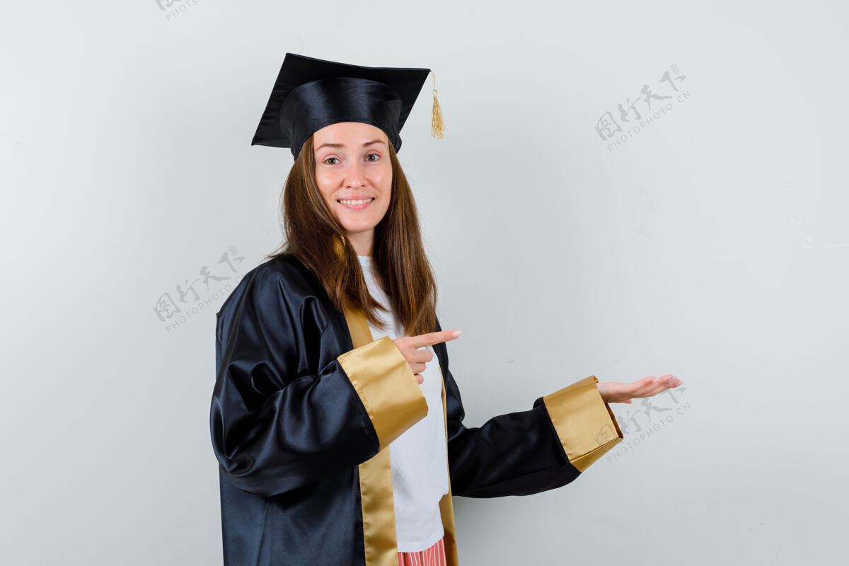 欢呼女毕业生指着右边 把手掌放在一边 穿着学院服 看上去很高兴正面视图旁白年轻大学