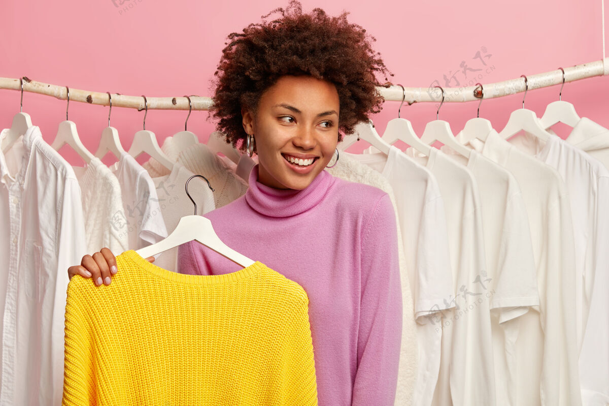 服装美丽快乐的女人在店里挑选衣服 高兴地看着旁边 把黄色的毛衣挂在衣架上购买买家挑选