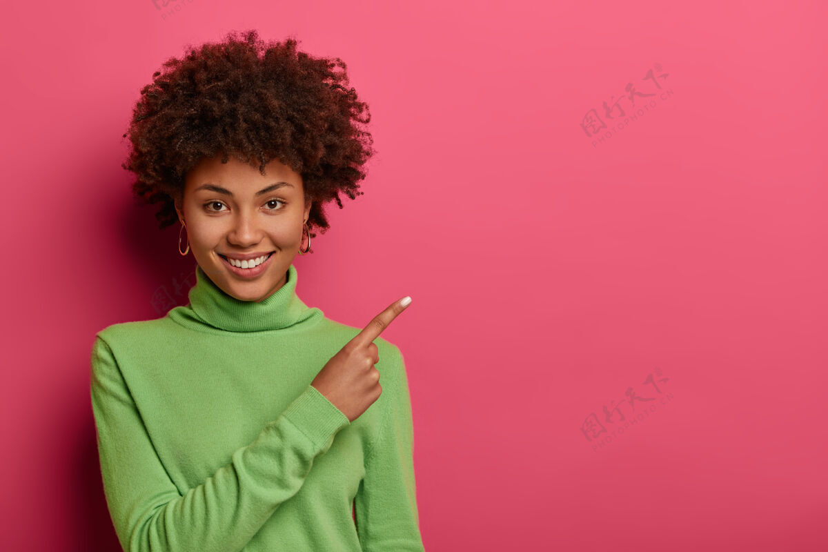 食指可爱的女人 卷发 健康的皮肤和洁白的牙齿 点在空白处 显示您的广告内容的空间姿势兴奋旁边