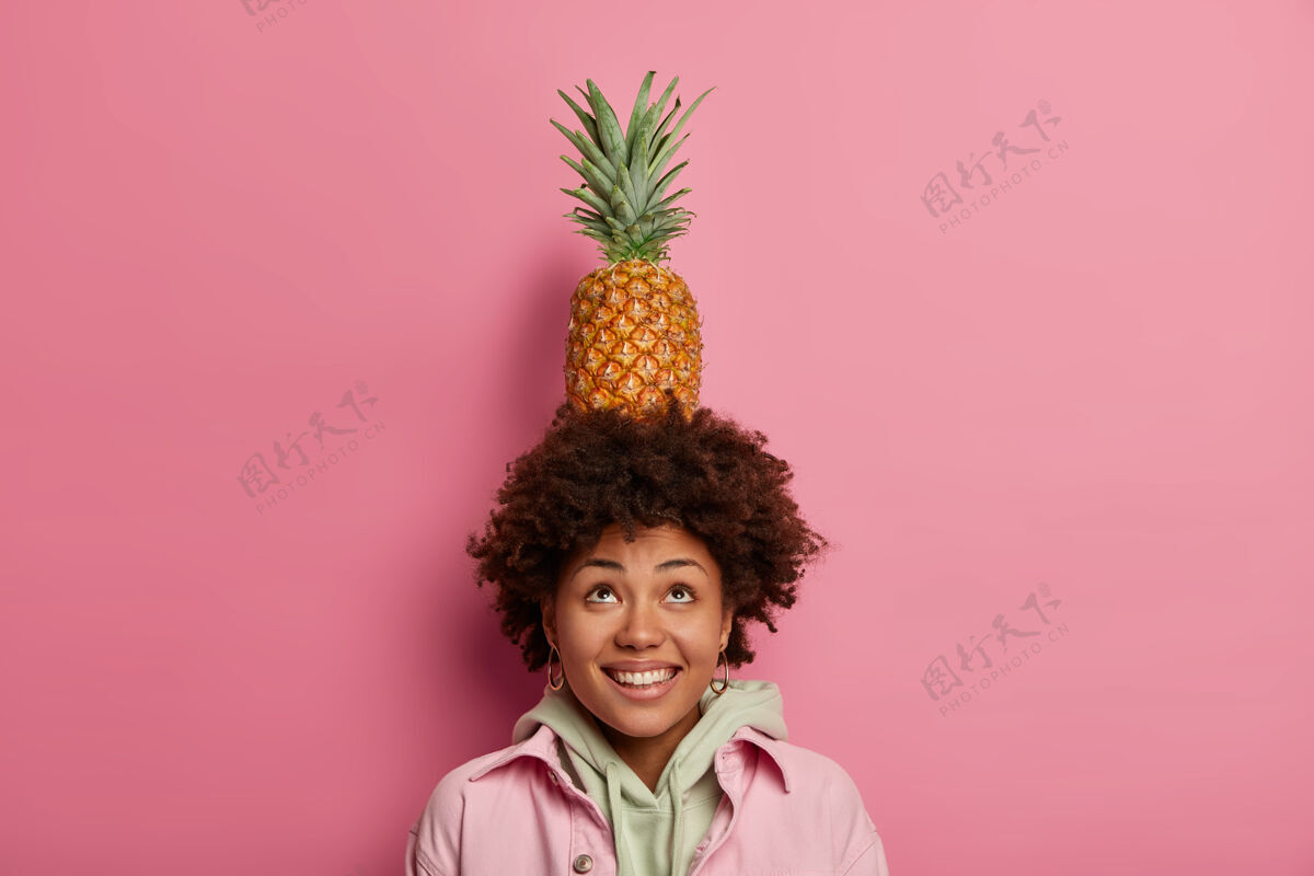 粉彩时尚少年头上抱着菠萝 用热带水果做把戏 抬头看 笑容灿烂 牙齿洁白 穿着连帽衫和夹克水果连帽衫菠萝