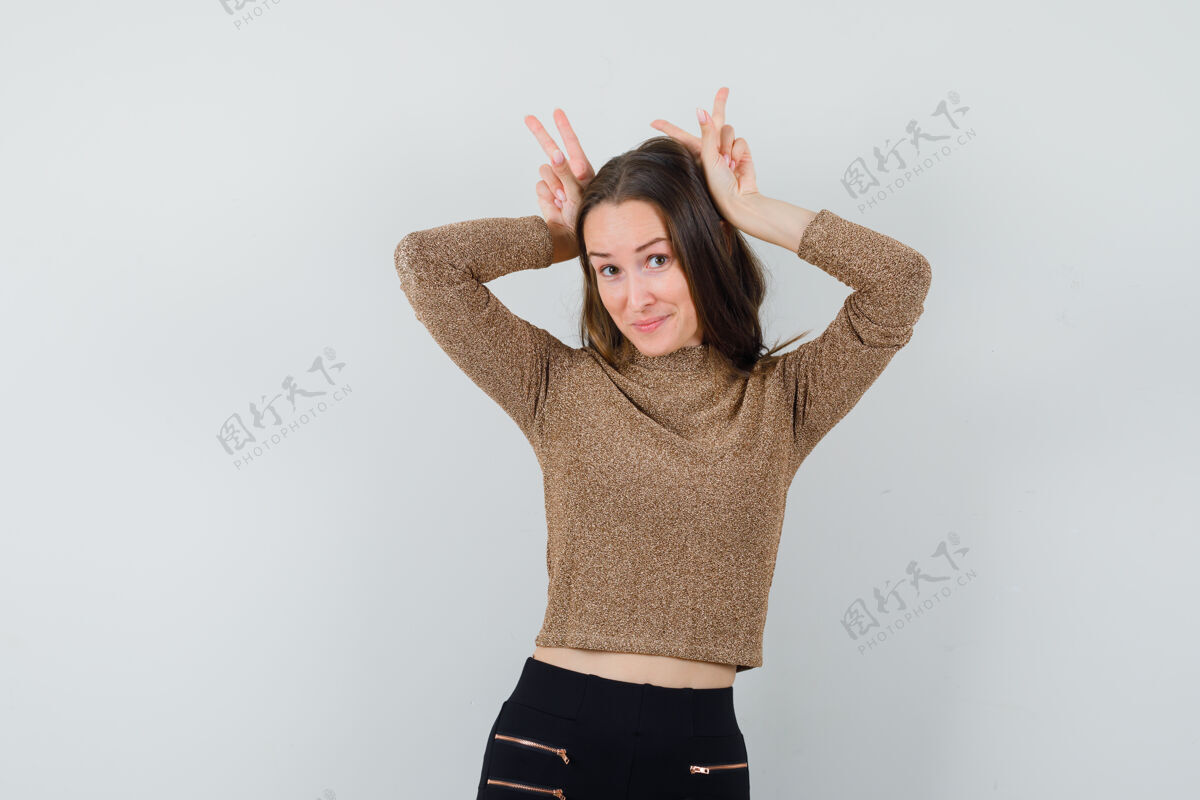 快乐年轻女子举手表示 在金色镀金毛衣和黑色裤子兔子的姿态 看起来很高兴前视图兔子女性手势