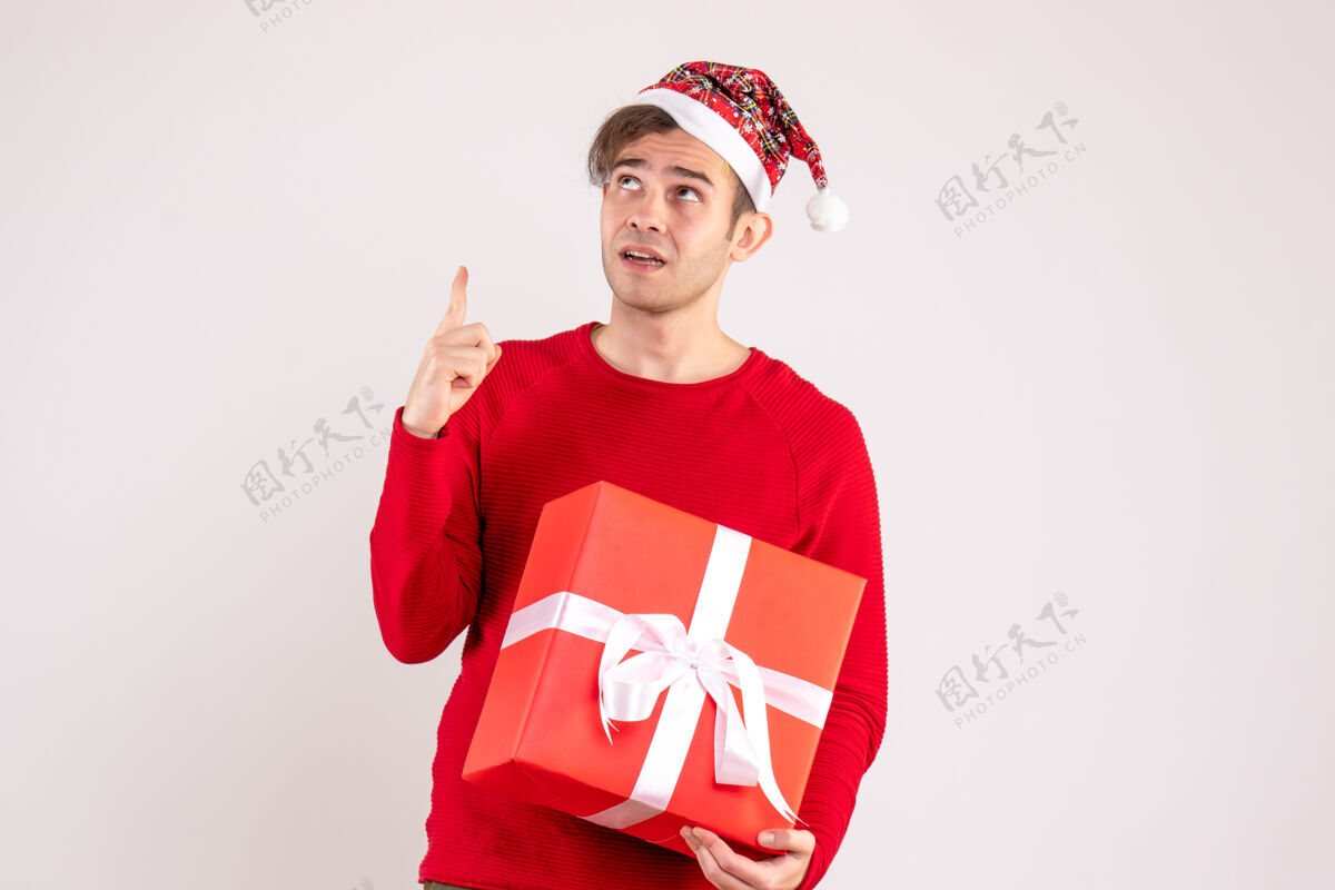 帽子前视图戴着圣诞帽的年轻人站在白色的背景上看着高处背景漂亮快乐