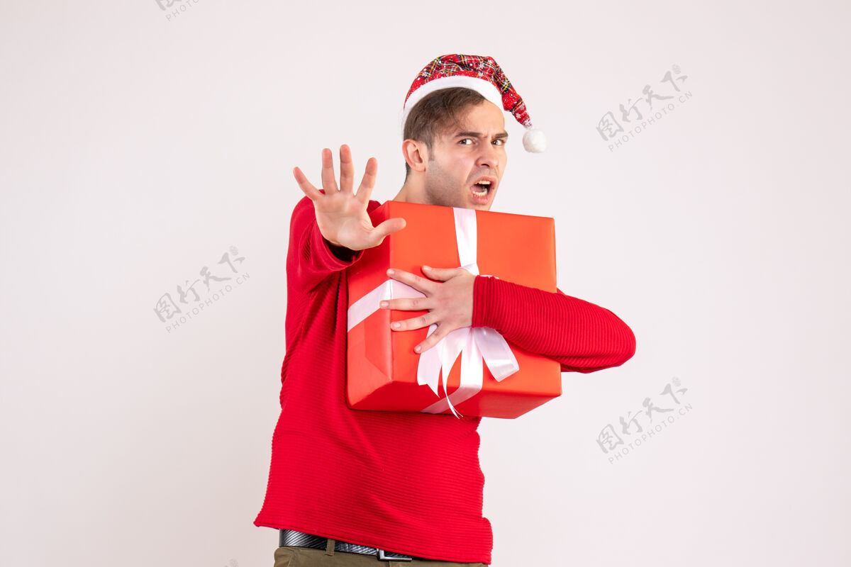 人正面图：戴着圣诞帽的年轻人拿着白色背景的礼物成人礼物年轻人