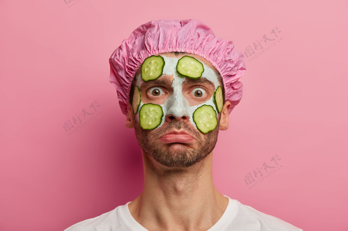 T恤不开心男人的横拍得到美容治疗 用蔬菜面膜提神 盯着镜头 戴着浴帽健康涂抹光滑