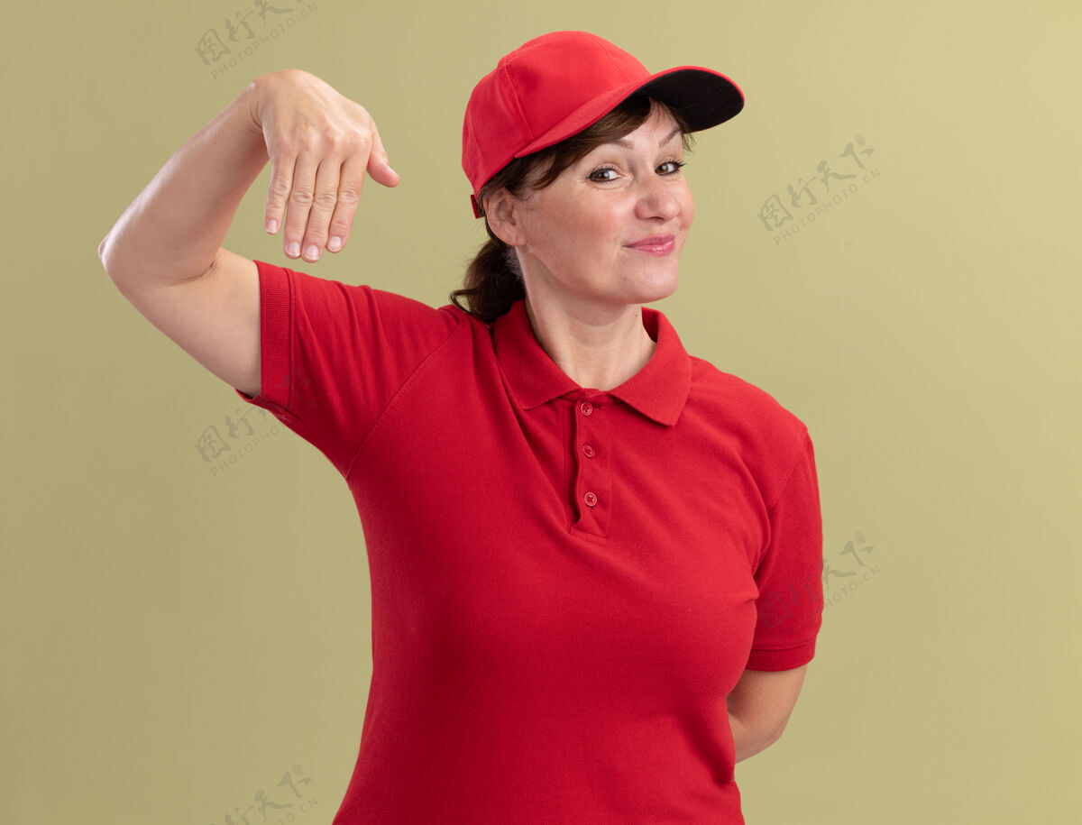 女人身穿红色制服 头戴鸭舌帽的中年女送货员站在绿色的墙上 双手自信地打着手势帽子年龄立场