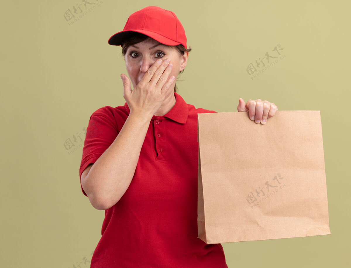 立场身穿红色制服 戴着礼帽的中年女送货员看着前面被震得捂着嘴站在绿色的墙上女人制服年龄