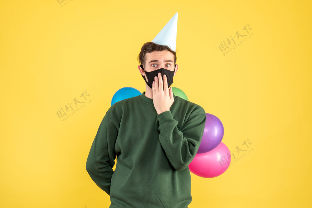 背景正面图：戴着派对帽 站在黄色背景上的彩色气球的年轻人行政人员聚会人物