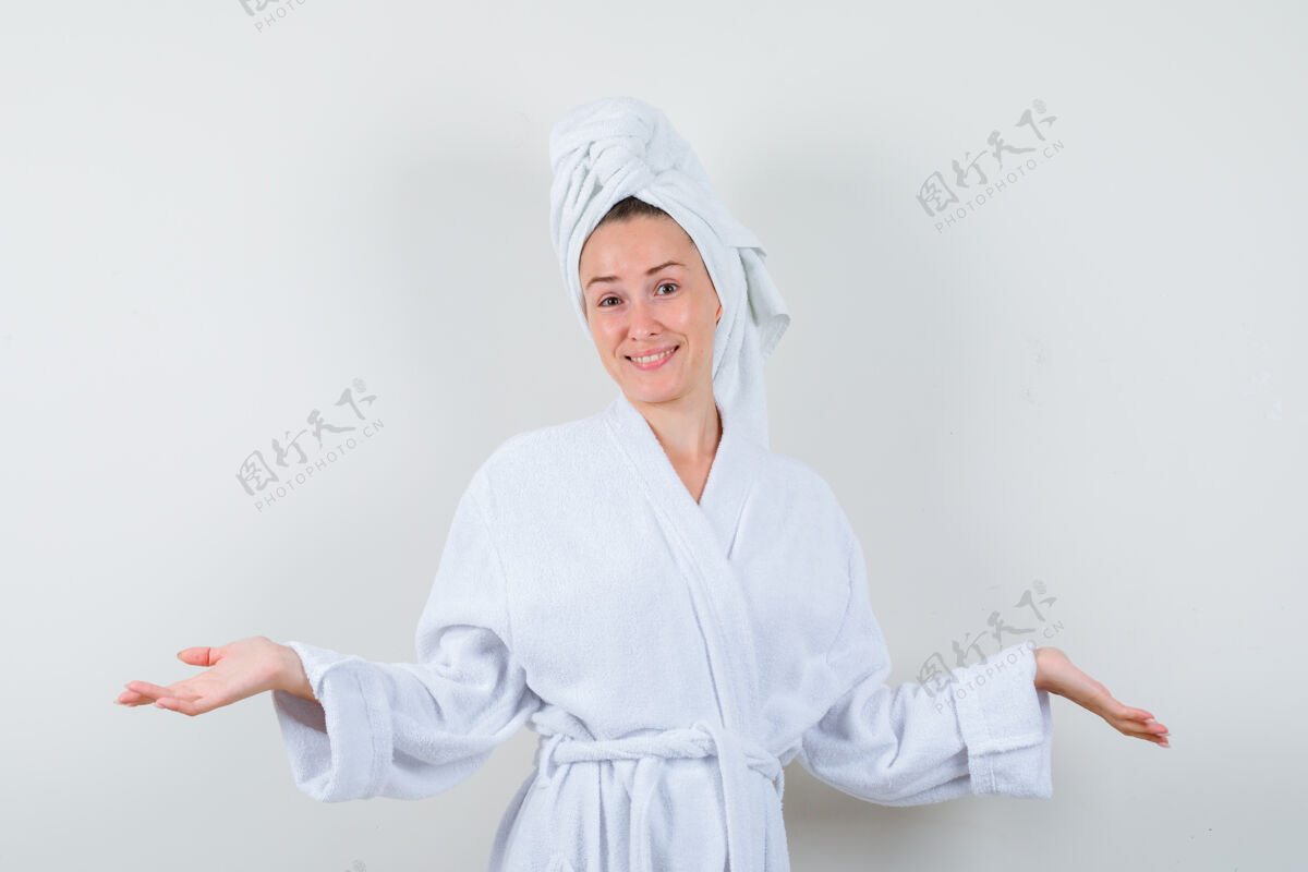 乐趣年轻女子摊开手掌 穿着白色浴衣 毛巾 看上去很高兴正面图模型前面成人