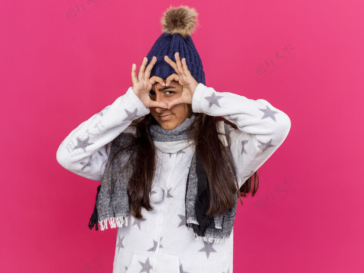 女孩可爱的生病的小女孩戴着冬天的帽子 戴着围巾 在粉红色的背景上显示出孤立的心的姿态显示手势疾病