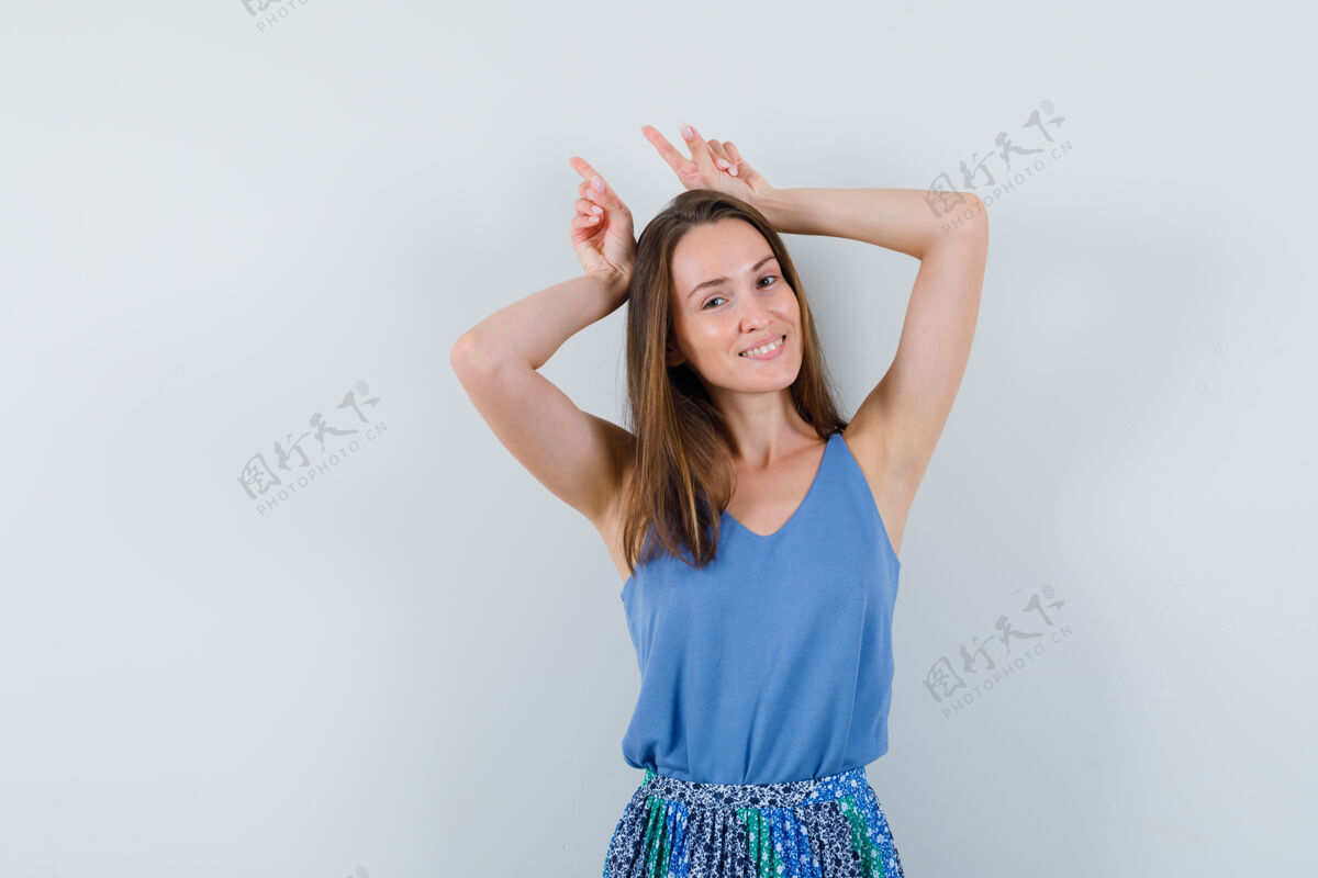 新鲜年轻的女士举着手指在头上作为牛角在单身 裙子和看起来很有趣黑发头发角