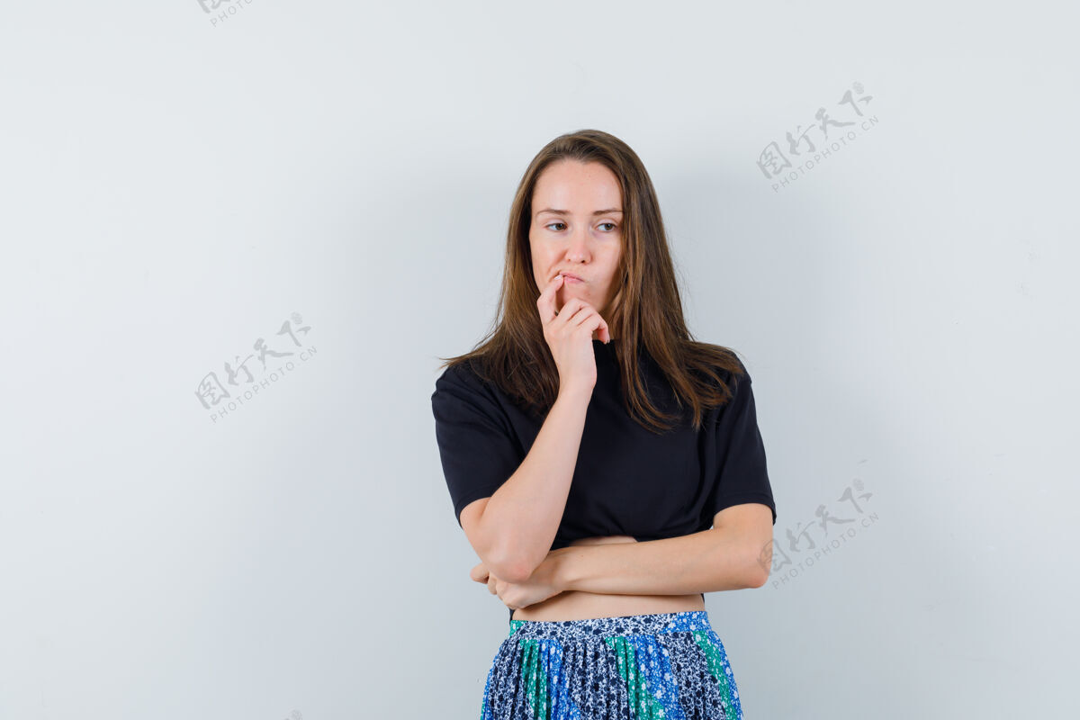 化妆年轻女子站在思考的姿势 看着在黑色的t恤和蓝色的裙子 看起来沉思思考健康干净