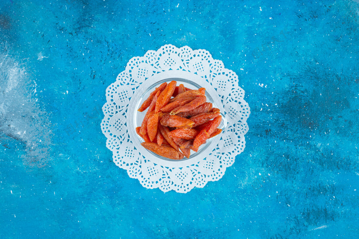 美味把杏干放在蓝色表面的杯垫上的碗里天然杏干美味