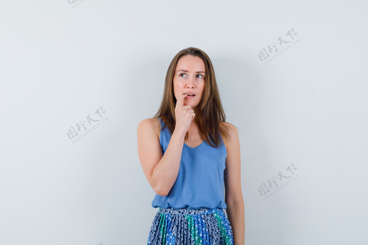 黑发年轻的女士咬着她的指甲在单身 裙子和看起来沉思女士新鲜裙子