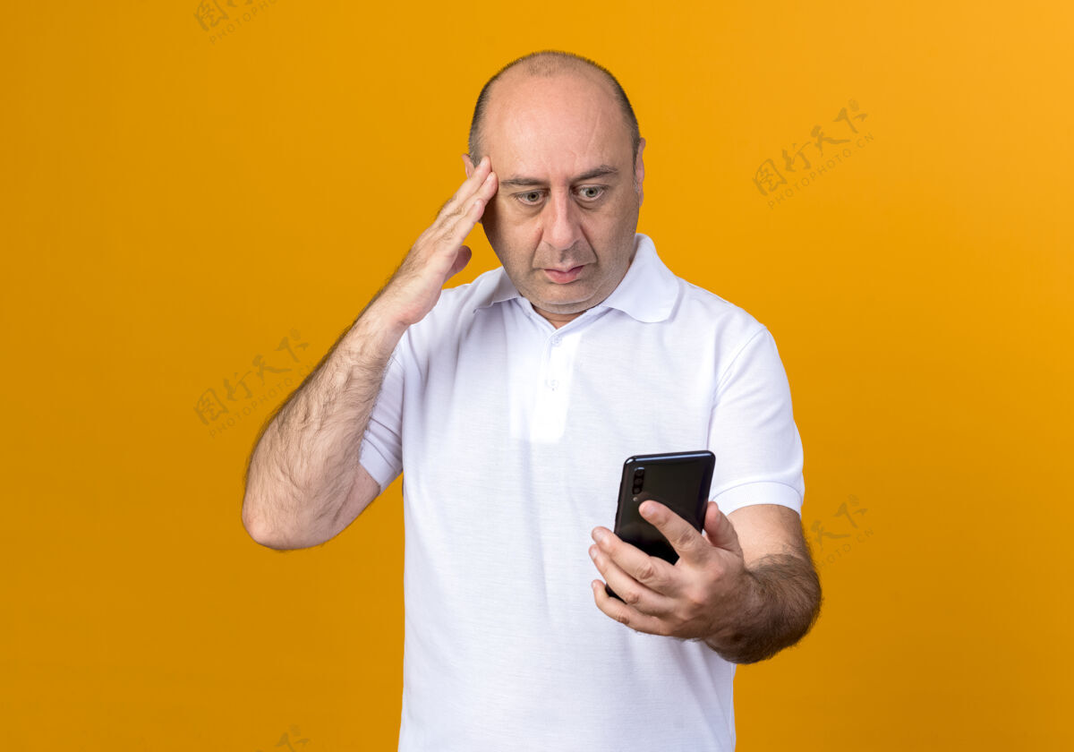 随意漫不经心的成熟男人拿着手机 看着放在太阳穴上的手孤立在黄色的背上手成熟电话