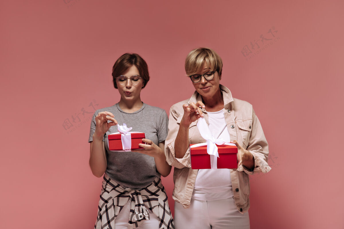 女士漂亮的两位女士 短发 穿着时髦的衣服 戴着一副很酷的眼镜 手里拿着红色的礼盒 在粉色的背景上解开带子夹克粉色白色