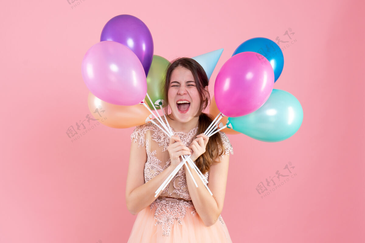 五颜六色前视图兴高采烈的聚会女孩与党帽举行气球接近她的脸脸乐趣生日