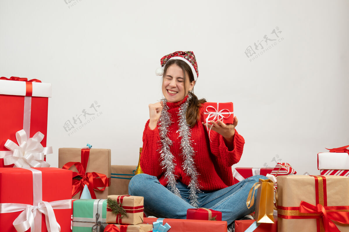 欢喜前视图兴高采烈的女孩与圣诞帽举行她的礼物 而高兴地坐在周围的礼物坐着礼物礼物