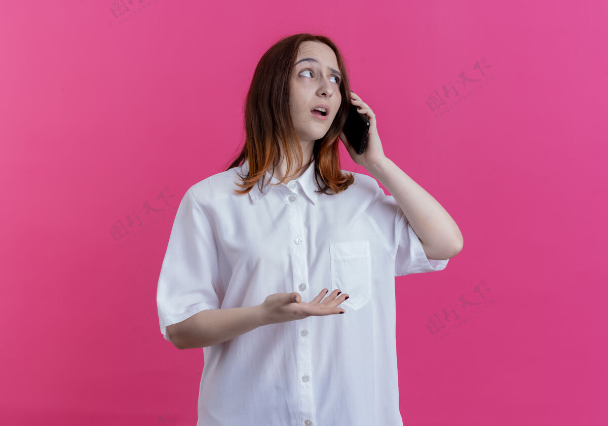 电话看着一边思考的年轻红发女孩在电话里说话 粉色背景上有一个单独的复制空间年轻思考女孩
