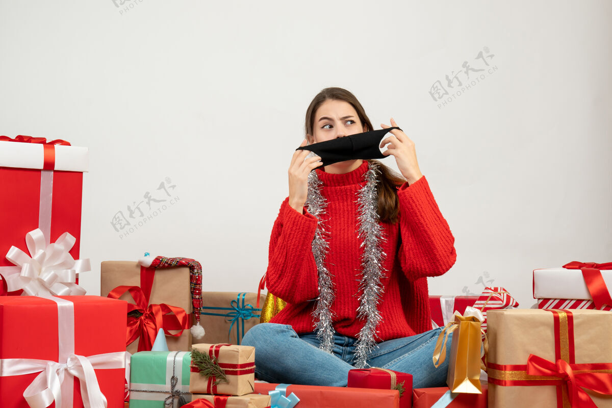 礼品前视图迷惑了一个穿着红毛衣的女孩 她摘下面具坐在礼物旁边围着时尚面具