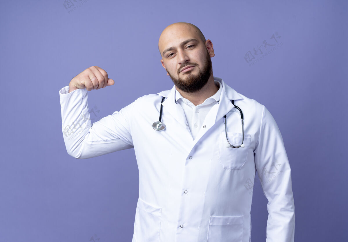手势自信的年轻秃头男医生穿着医用长袍和听诊器做着强烈的手势隔离在蓝色背景上医生年轻男性